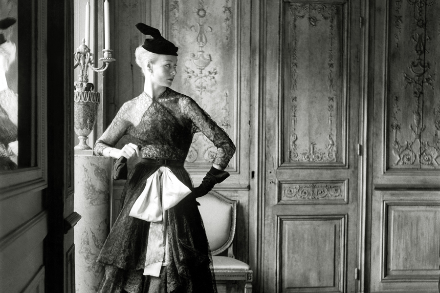 ca. 1951 --- Original caption: Woman modeling black lace dress with pink sash copied from Balenciaga, with hat and gloves. --- Image by © Condé Nast Archive/Corbis